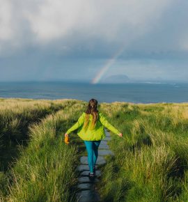Rear view of female contemplating the trip on beautiful island with bright rainbow in the sky in Scandinavia